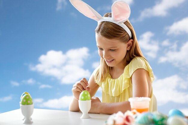 Fille heureuse colorant des œufs de Pâques sur le ciel bleu