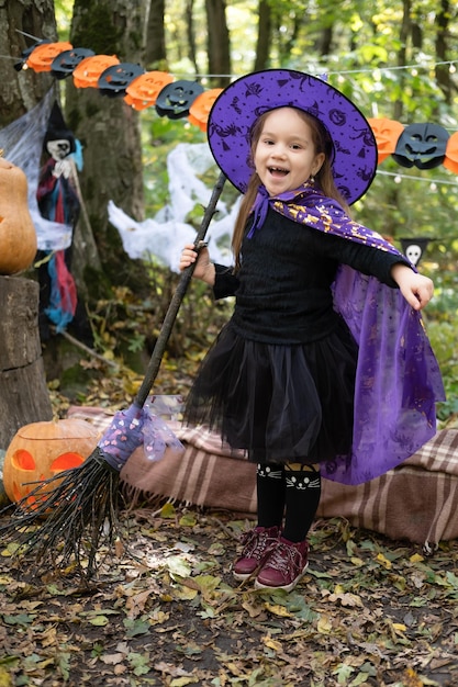 fille heureuse en costume d'halloween et chapeau de sorcière avec balai dans la décoration d'halloween en plein air