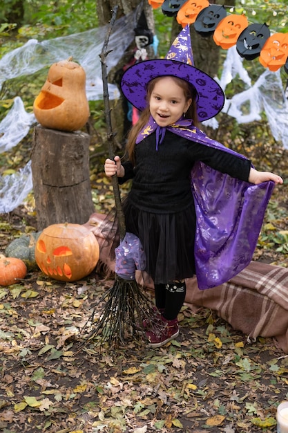 fille heureuse en costume d'halloween et chapeau de sorcière avec balai dans la décoration d'halloween en plein air