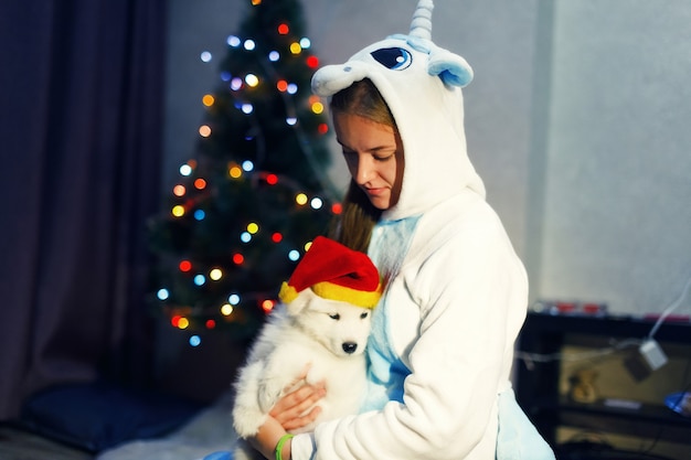 Fille heureuse en costume de licorne avec chien husky samoyède dans les décorations de Noël