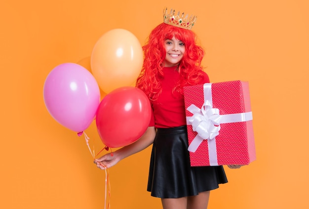 Fille heureuse en couronne avec boîte cadeau et ballon de fête sur fond jaune