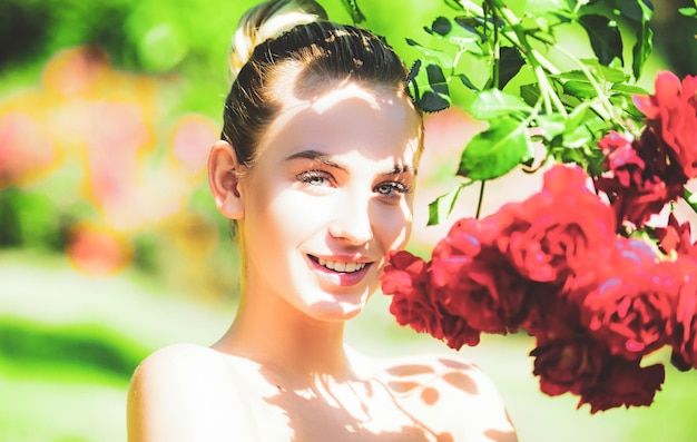 Fille heureuse dans un jardin avec des roses rouges belle jeune femme sentant une fleur rose