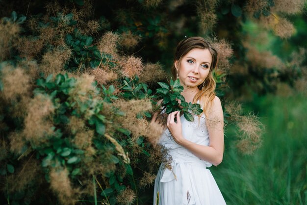 Fille heureuse dans une longue robe turquoise dans un parc verdoyant sur fond d'herbes, d'arbres et de rosiers