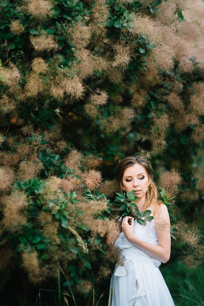 Fille heureuse dans une longue robe turquoise dans un parc verdoyant sur fond d'herbes, d'arbres et de rosiers