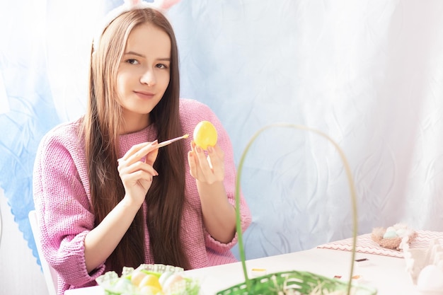 Une fille heureuse dans les oreilles de lapin peint des oeufs de Pâques pour les vacances a des sourires amusants met dans un panier