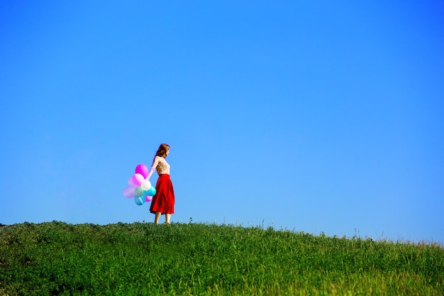 Fille heureuse dans les prés toscans avec des ballons colorés, contre le ciel bleu et le pré vert. Toscane, Italie