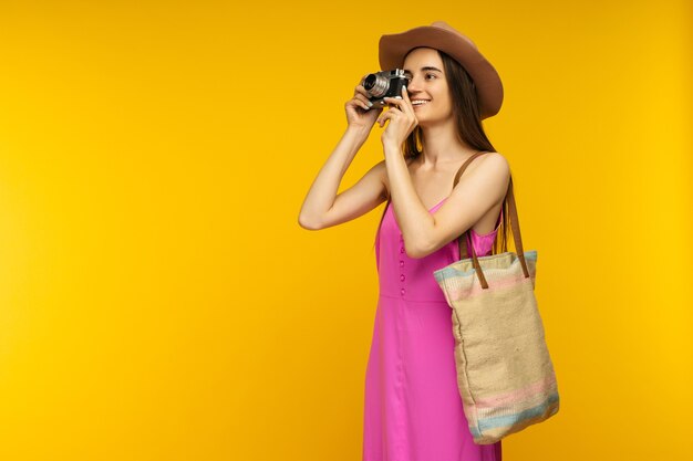 Fille heureuse dans une robe rose et des lunettes de soleil tenant la caméra sur une image jaune-