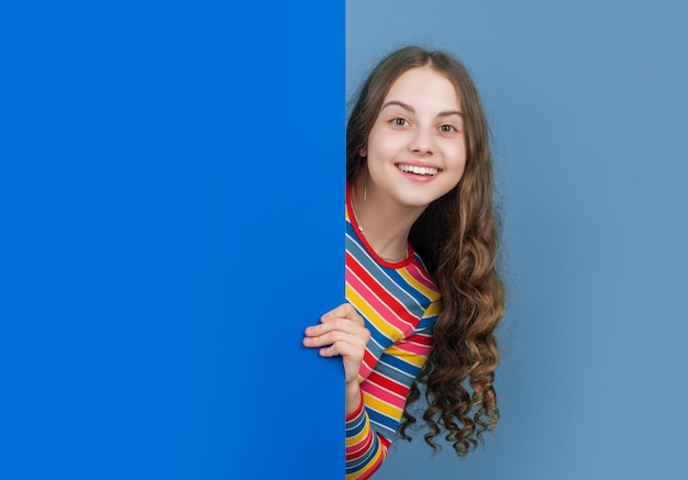 Photo fille heureuse derrière un papier bleu blanc avec un espace de copie pour la publicité