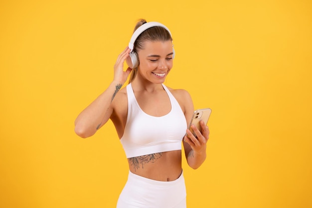 Fille heureuse en écoutant de la musique dans des écouteurs adaptés à votre corps playlist pour la formation formation application mobile fitness application smartphone sport femme a entraînement en ligne vie saine