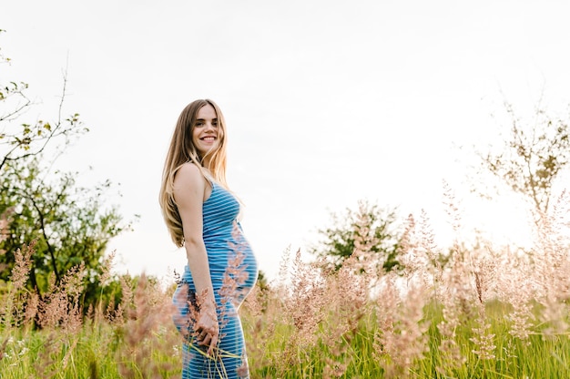 Fille heureuse enceinte se tenir debout sur l'herbe de fond surpasser. demi-longueur, moitié supérieure. reculer. Fermer. le vent souffle les cheveux.