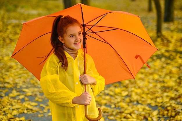 Fille heureuse d'enfant avec un parapluie et des bottes en caoutchouc sur une promenade d'automne