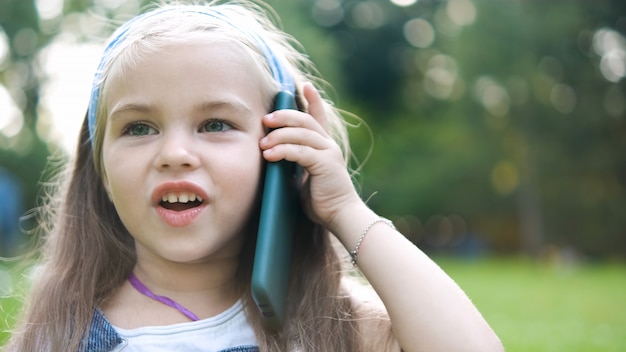 Fille heureuse d'enfant parlant au téléphone portable dans le parc d'été.