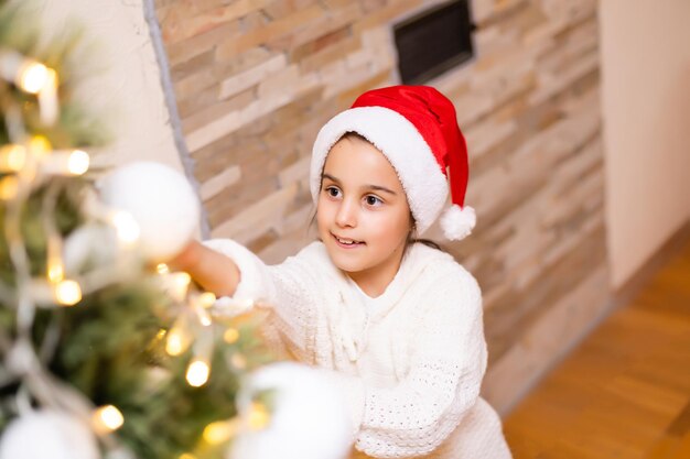 Fille heureuse d'enfant riant dans la chambre au-dessus de l'arbre de Noël. Porter un pull élégant. Enfance. Période de Noël.