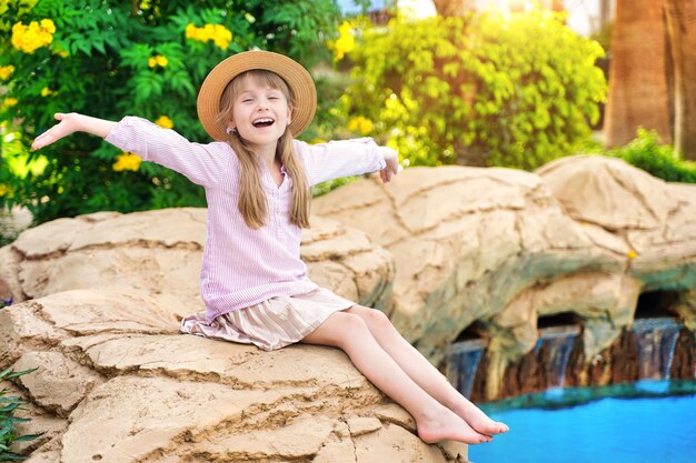 La fille heureuse d'enfant se réjouit au soleil et à la piscine d'été et aux feuilles de palmier autour de l'égypte d'hôtel