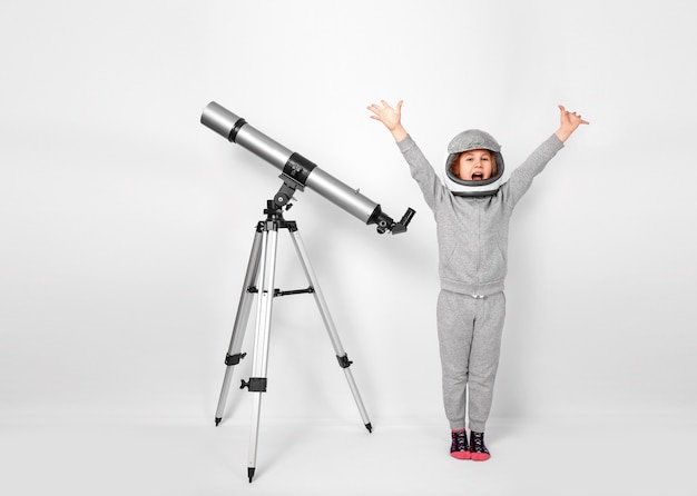 Fille heureuse d'enfant vêtue d'un costume d'astronaute debout à côté du télescope.