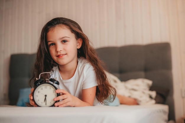 Photo une fille heureuse est allongée sur le lit et tient un réveil