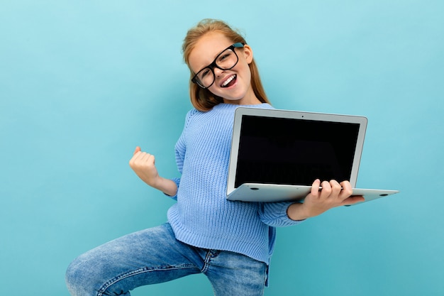 Fille heureuse excitée sur fond bleu avec un ordinateur portable, gestes ok