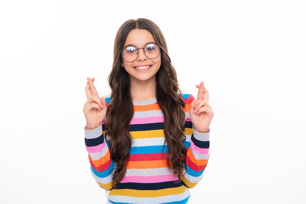 Fille heureuse face à des émotions positives et souriantes Enfant adolescent tenant les doigts croisés pour la bonne chance Portrait d'une fille joyeuse prie et espère que les rêves deviennent réalité isolés sur fond de studio blanc