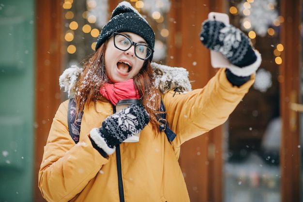 Fille heureuse fait un selfie dans la ville d'hiver. Fille fait selfie en hiver et rue gelée