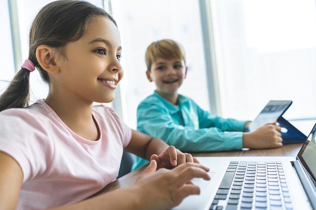 La fille heureuse et un garçon assis à la table avec un ordinateur portable et une tablette