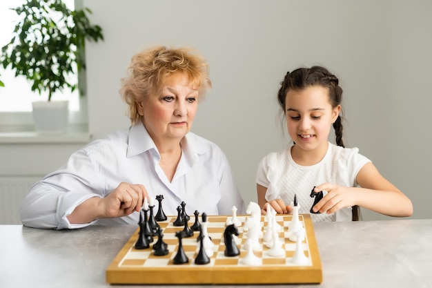 Fille heureuse avec grand-mère assise à la table et jouant aux échecs.