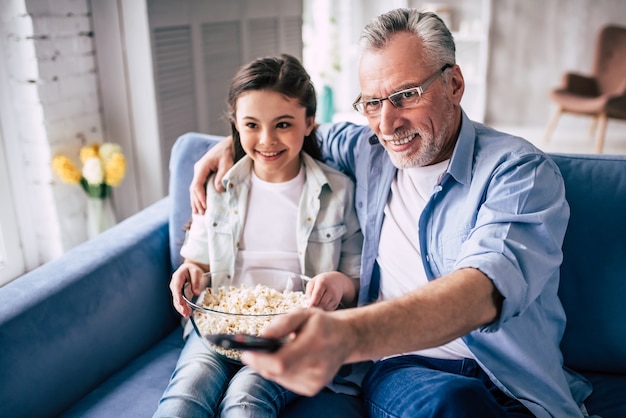 La fille heureuse et un grand-père regardant la télévision avec un pop-corn