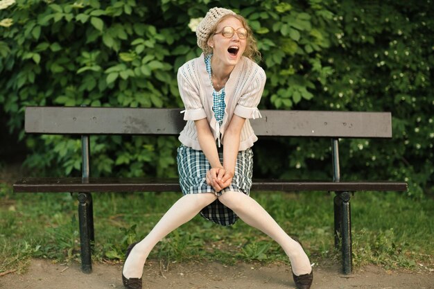 une fille heureuse et heureuse est assise sur un banc dans le parc et sourit et crie