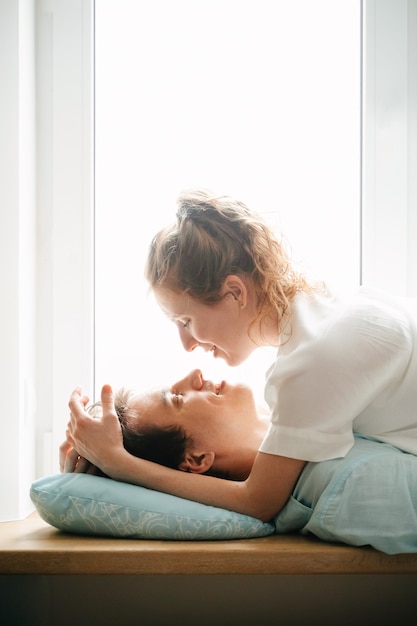 Fille heureuse et homme étreignant près de la fenêtre à la maison. Vêtements blancs et bleus. Saint Valentin.