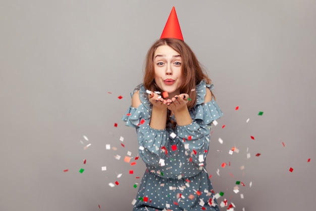 Fille heureuse insouciante avec un chapeau de fête soufflant des paillettes, souriant appréciant la célébration de l'anniversaire