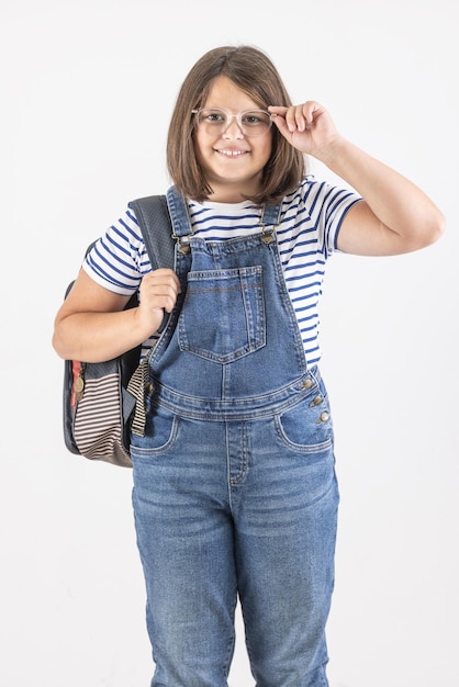 Une fille heureuse à lunettes porte un sac à dos et une tenue d'école décontractée