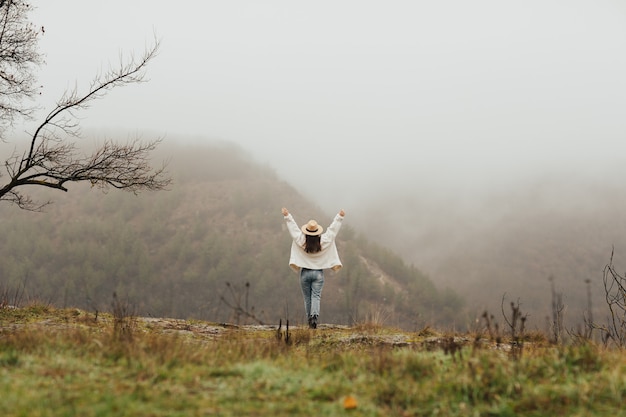 Fille heureuse avec les mains en l'air bénéficie d'une vue idyllique sur la montagne brumeuse.