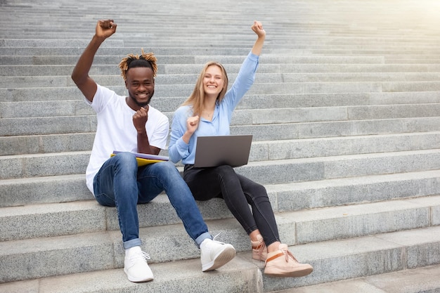 Fille heureuse et mec assis dans les escaliers dans le parc étudiant à l'extérieur en souriant regardant une caméra