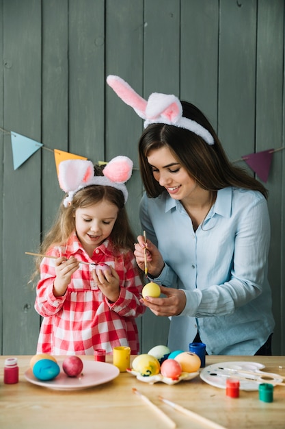 Fille heureuse et mère dans les oreilles de lapin peignant des oeufs pour Pâques