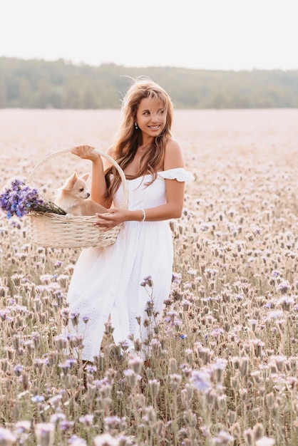 Fille heureuse avec mignon chien Chihuahua dans un panier avec un bouquet de fleurs dans la nature sur le terrain en été