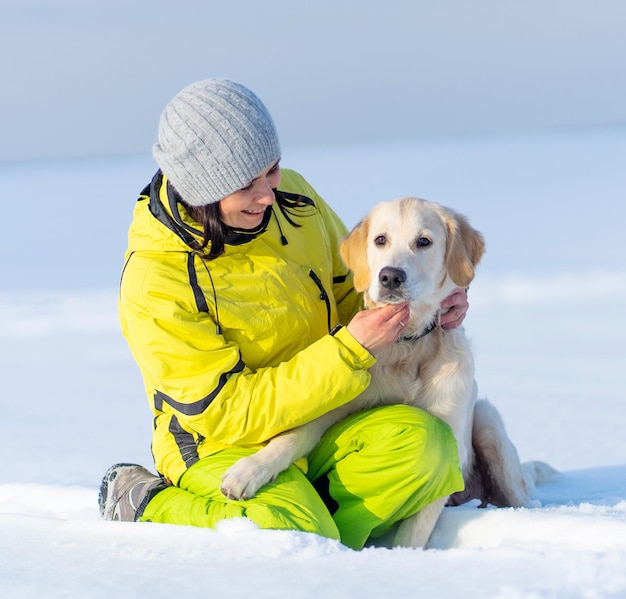 Fille heureuse avec mignon jeune chien golden retriever assis dans la neige