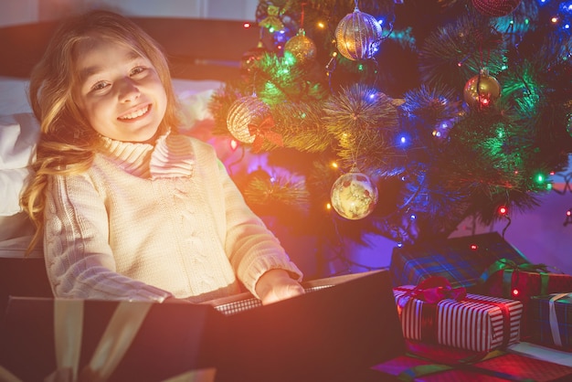 La fille heureuse ouvre la boîte à lumière près de l'arbre de Noël. le soir la nuit