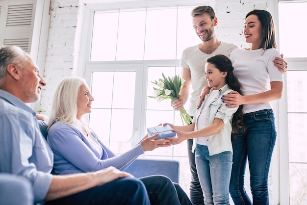 La fille heureuse avec des parents donnant un cadeau avec des fleurs aux grands-parents