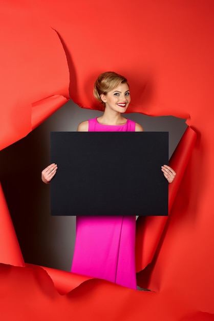 Photo une fille heureuse passe à travers un trou dans un modèle blond sensuel en papier rouge en robe rose tient un noir vide