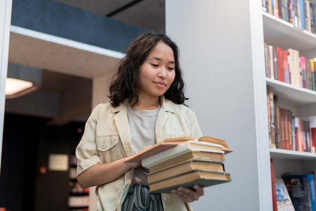 Fille heureuse avec une pile de livres lisant l'un d'entre eux