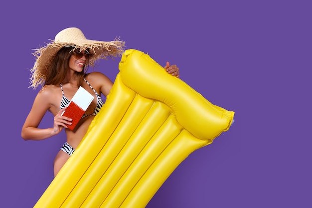 Une fille heureuse prête pour les vacances d'été se tient avec un matelas gonflable jaune et détient un passeport pour les billets
