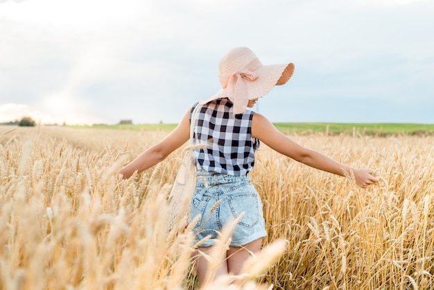 Fille heureuse qui marche dans le blé doré, avec son dos, mode de vie en plein air. Concept de liberté.