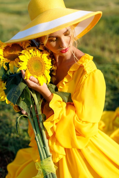 une fille heureuse en robe jaune tient des fleurs de tournesol dans un champ de tournesols contre le ciel