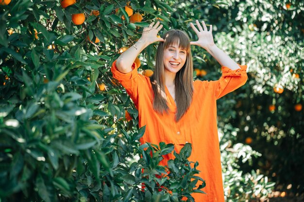 Une fille heureuse en robe orange montre une drôle de démarche en se tenant la main autour de la tête dans un jardin orange