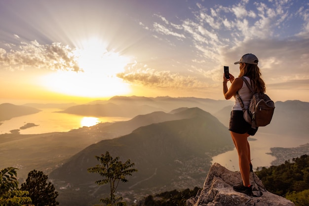Une fille heureuse avec un sac à dos photographie les paysages marins du monténégro depuis le sommet de la montagne