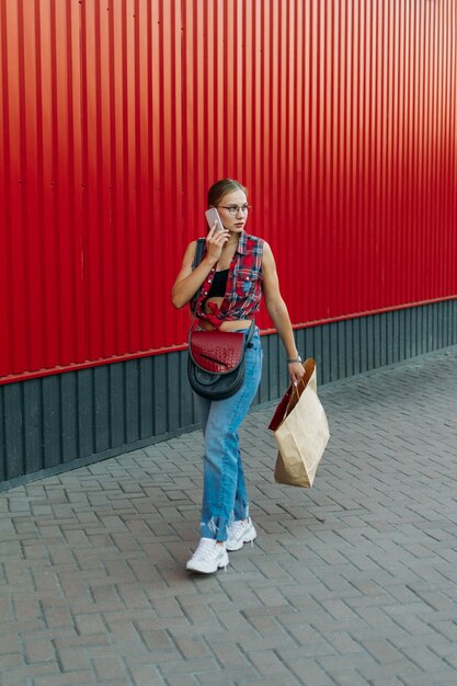 Fille heureuse avec un sac en papier sur fond de magasin mur rouge jeune femme tenant un sac plein