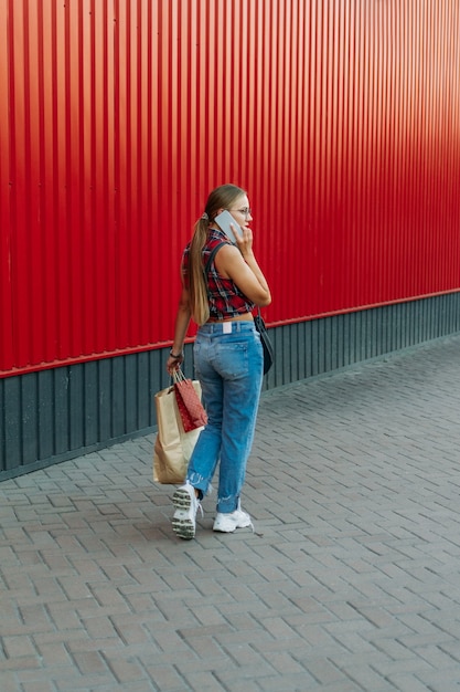 Fille heureuse avec un sac en papier sur fond de magasin mur rouge jeune femme tenant un sac plein