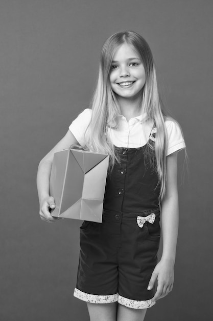 Fille heureuse avec sac à provisions sur fond violet Petit sourire accro du shopping avec sac en papier Enfant shopper souriant avec achat Préparation et célébration des fêtes Shopping et vente