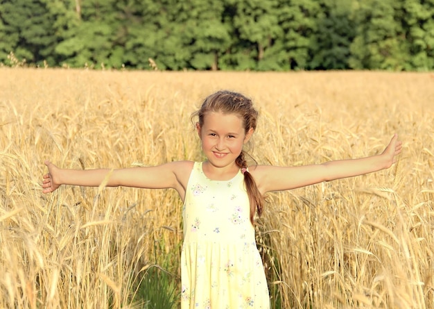 une fille heureuse se tient sur le terrain avec ses bras grands ouverts