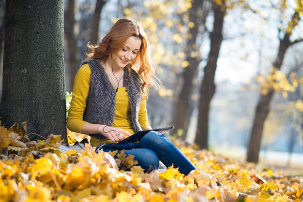 Fille heureuse avec une tablette dans le parc d'automne avec des feuilles jaunes