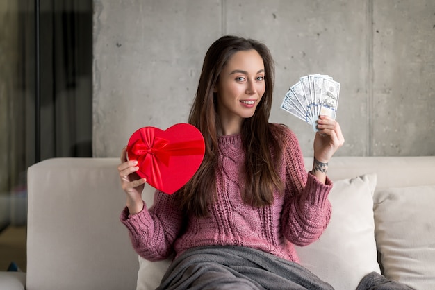 fille heureuse tenant un cadeau en forme de coeur et des billets d'un dollar